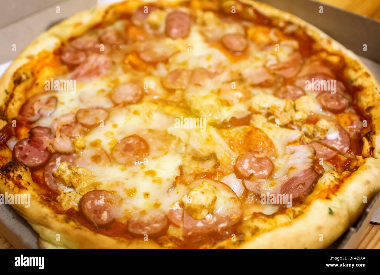 Una pizza appena sfornata con formaggio fuso, salsiccia e prosciutto in una scatola di cartone, che illustra il fast food, la consegna e i pasti deliziosi Foto Stock
