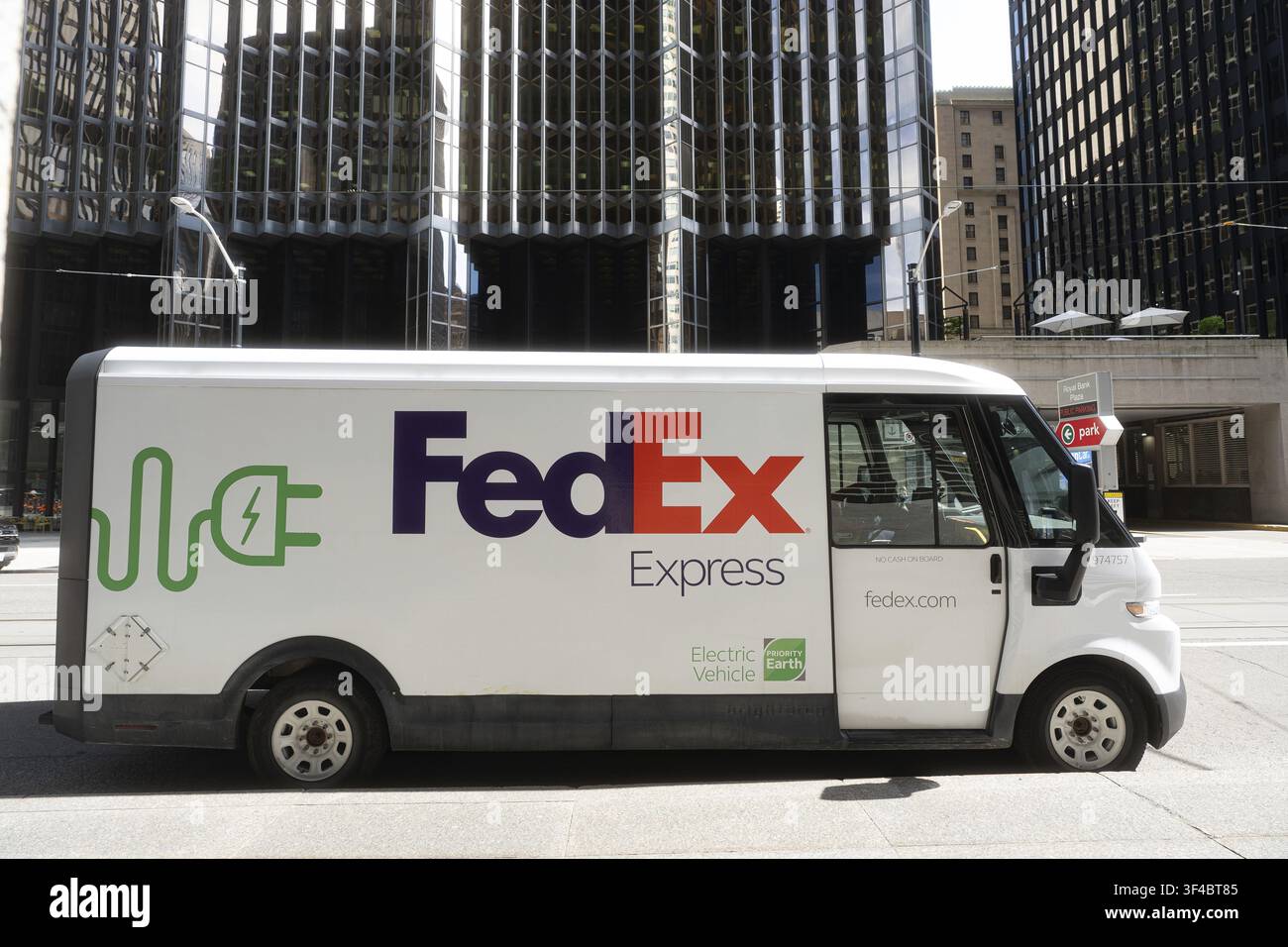 Un furgone elettrico di consegna FedEx Express è parcheggiato su una strada cittadina nel centro di Toronto, circondato da edifici moderni per uffici. Il furgone presenta in modo evidente Foto Stock