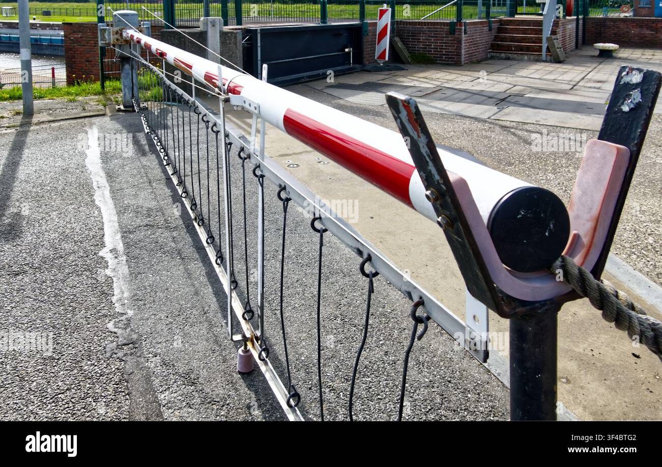 Braccio barriera con strisce rosse e bianche, che chiude il passaggio, con una corda che ne assicura l'estremità, rappresentante sicurezza e ritardo Foto Stock