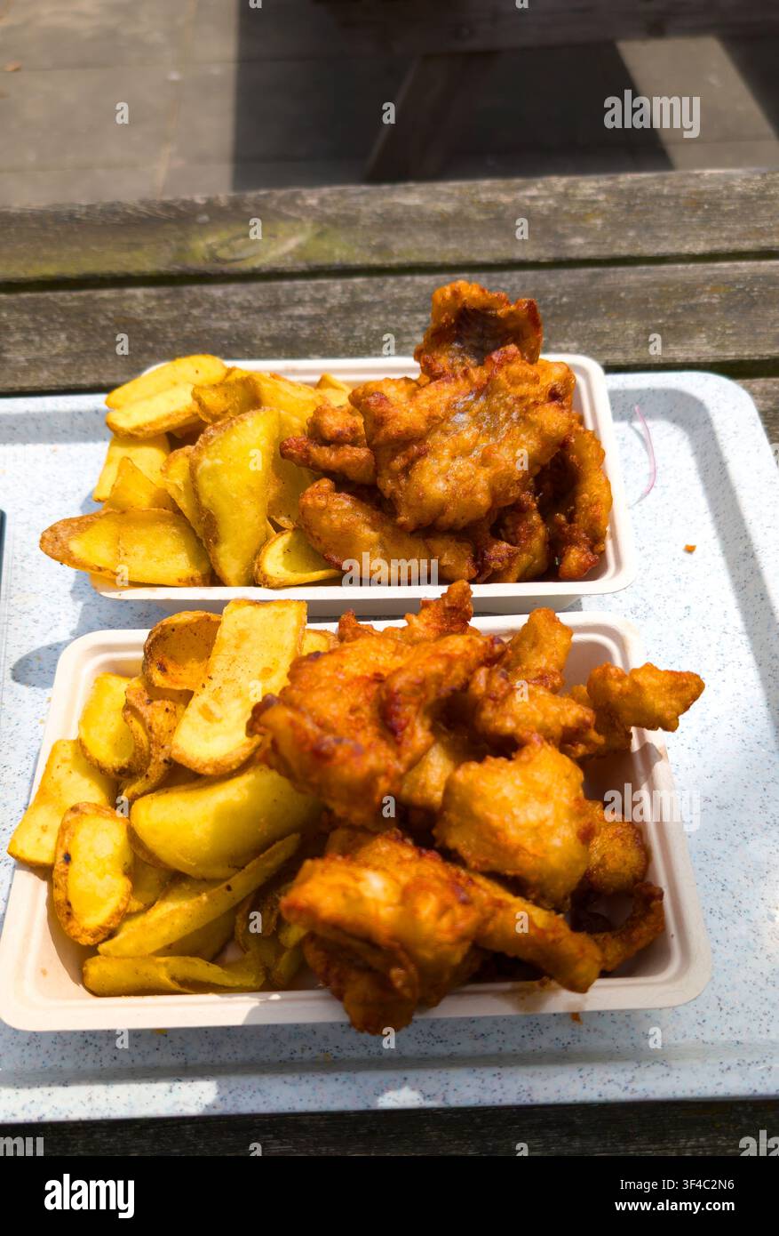 Pesce e patatine croccanti in vassoi da asporto su una panca di legno all'aperto – pasto pranzo fritto dorato Foto Stock
