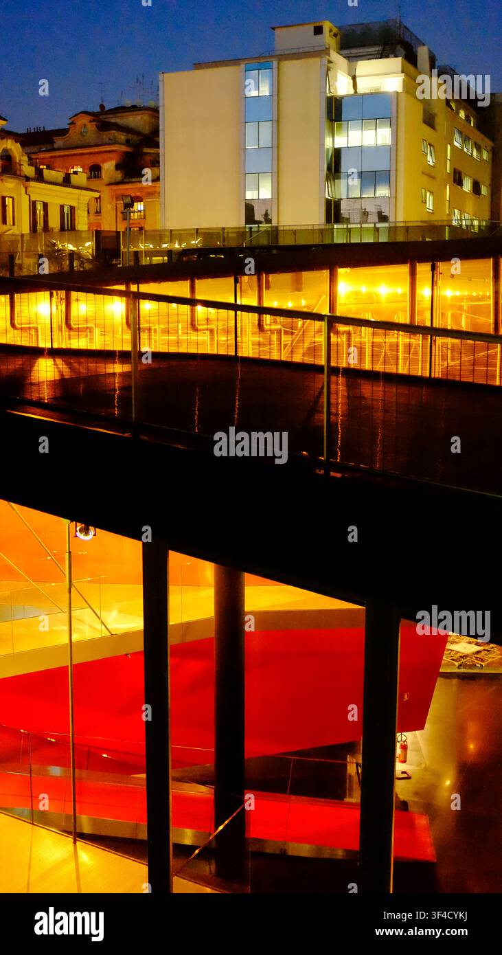 Vista dalla terrazza sul tetto che mostra la facciata in vetro con strutture interne rosse e rampa illuminata all'interno del Museo MACRO. Roma, Italia. Foto Stock