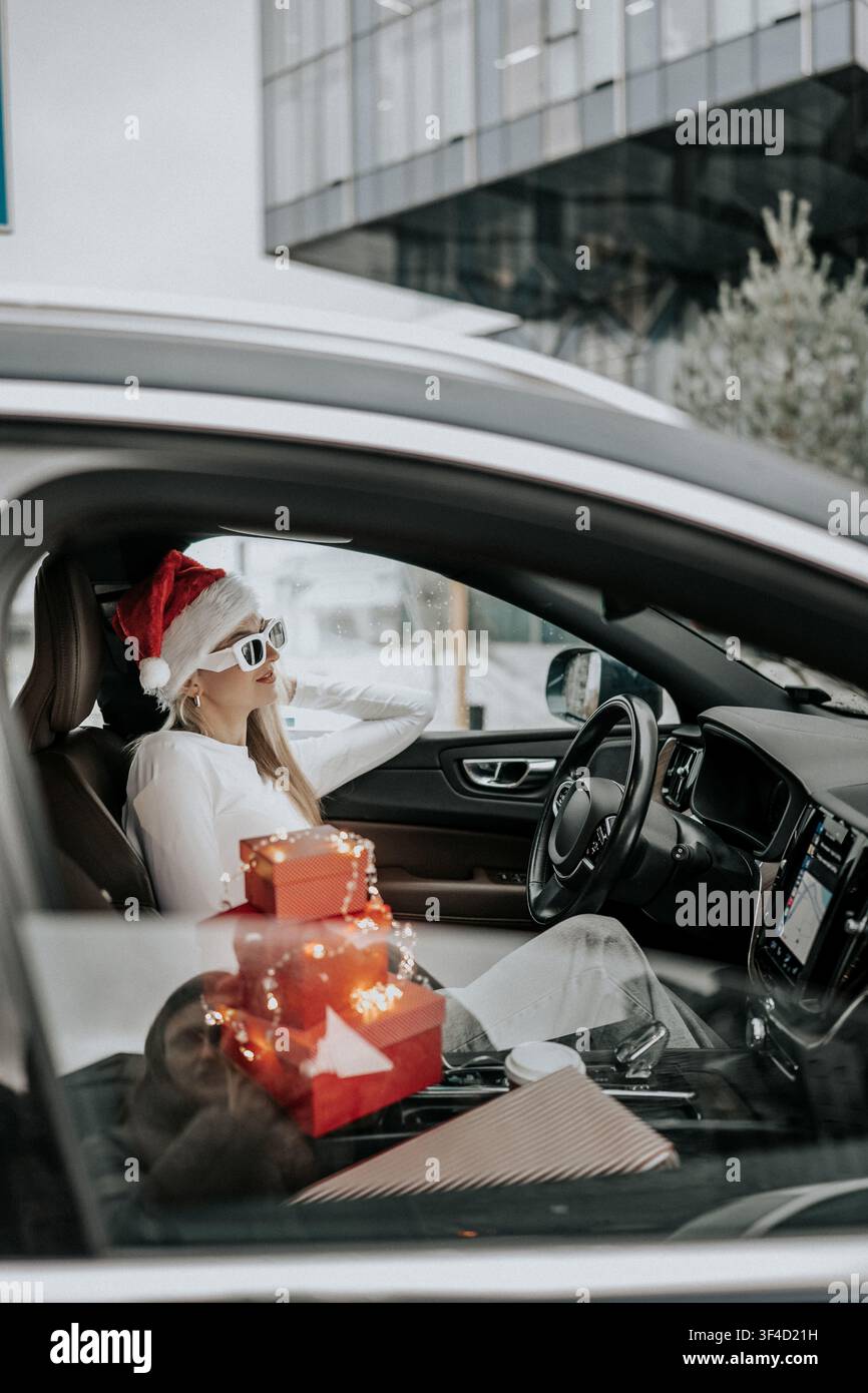 Donna con cappello di Babbo Natale seduta in un'auto circondata da regali durante la stagione festiva Foto Stock