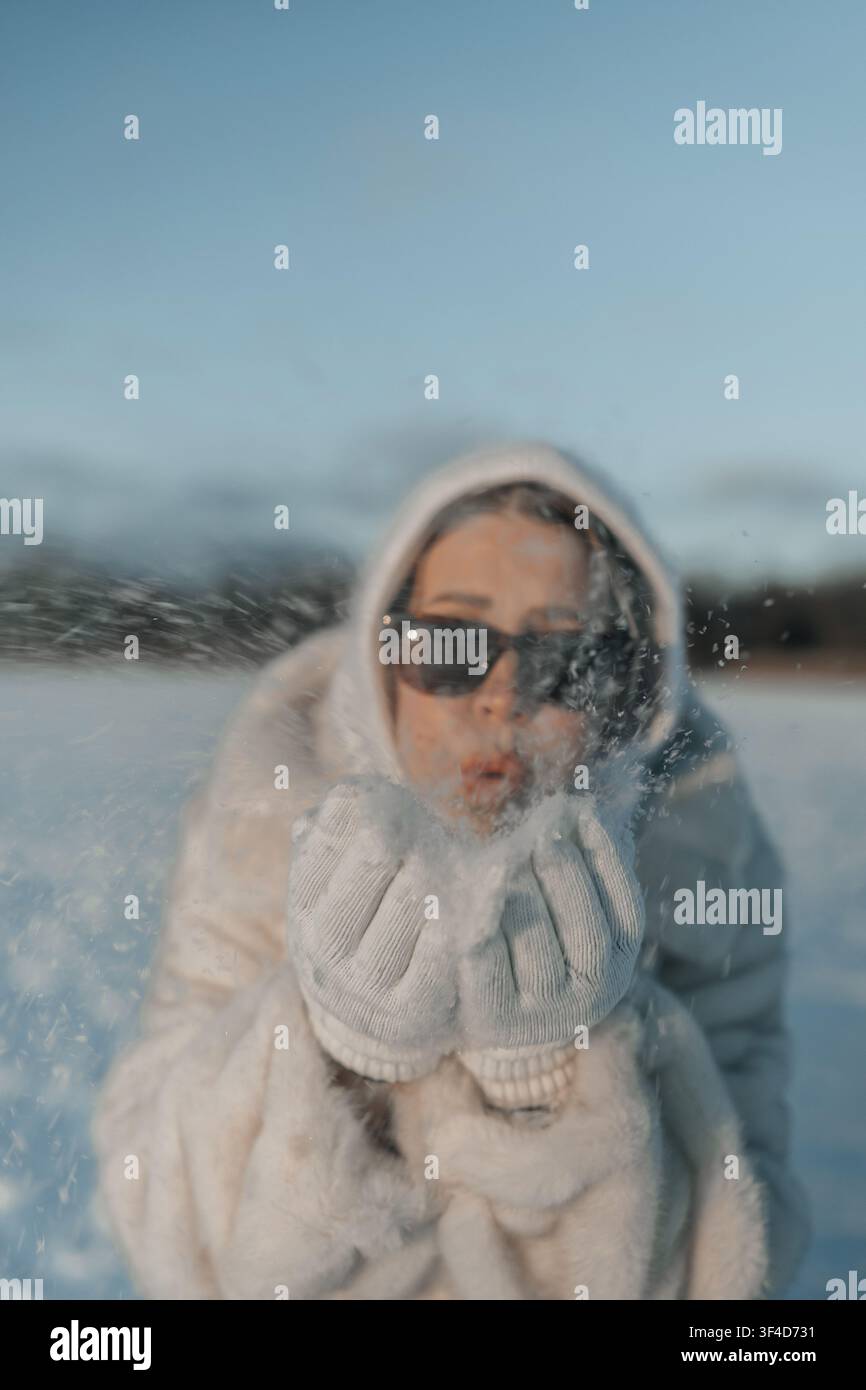 Donna che soffia neve in un paesaggio innevato in una limpida giornata invernale con luce solare intensa Foto Stock