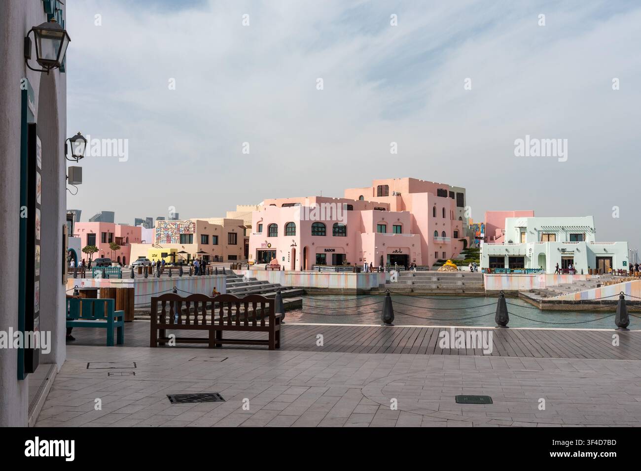 Doha, Qatar - 1 febbraio 2026: Vista ampia a livello degli occhi di edifici in stile mediterraneo dai colori pastello, una passerella in legno. Foto Stock