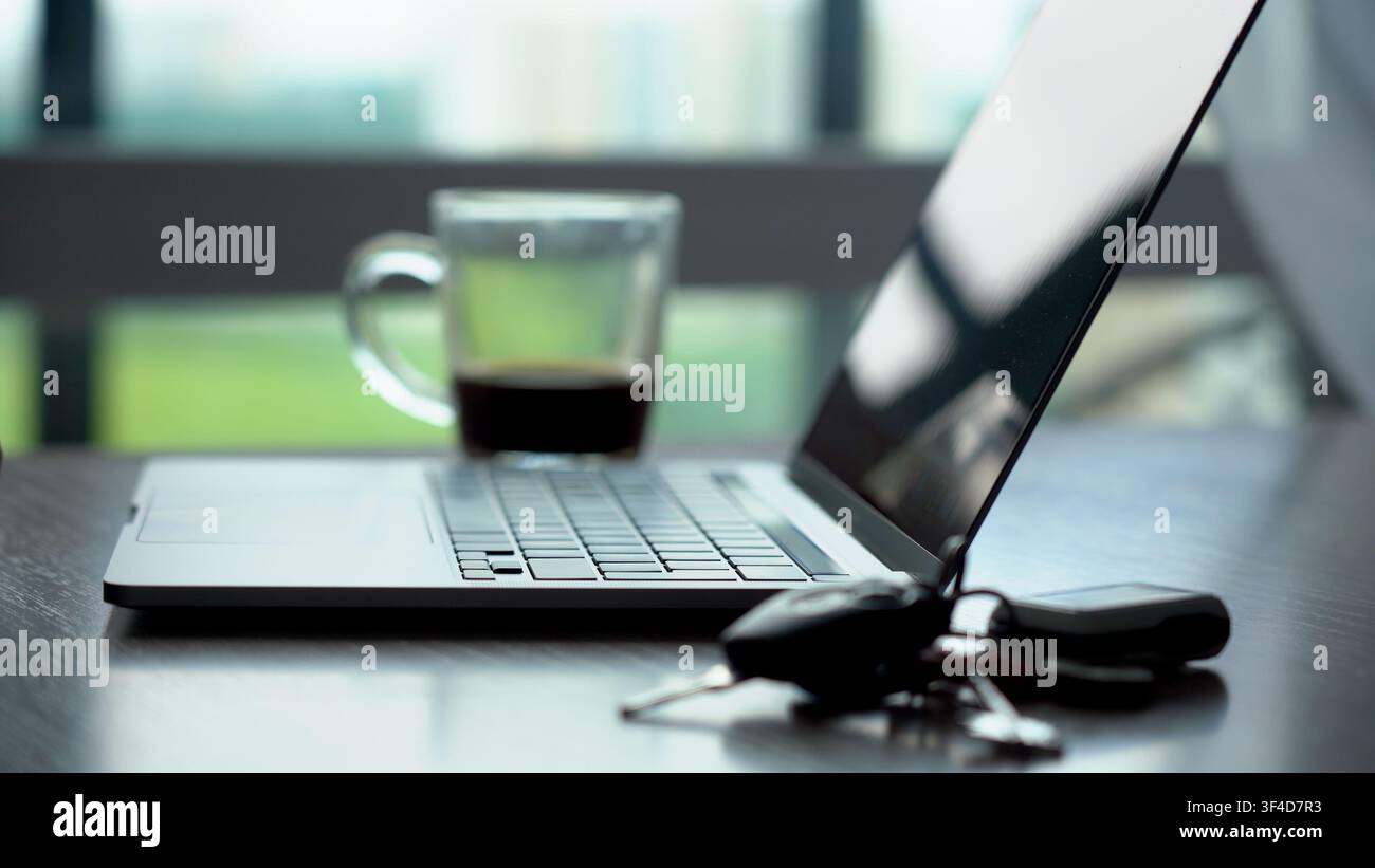 Uno spazio di lavoro contemporaneo con un laptop, caffè e chiavi, che cattura l'essenza della produttività moderna e del minimalismo. Foto Stock