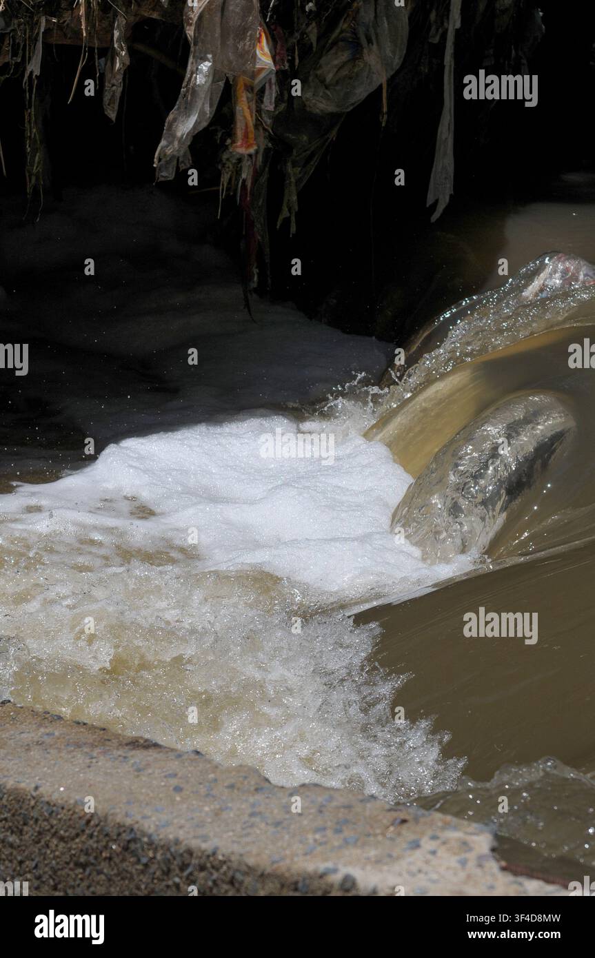 Acqua schiumosa inquinata e detriti di plastica che fluiscono da uno scarico pluviale nel fiume Hennops nel Gauteng, Sudafrica, illustrando il deflusso urbano, wa Foto Stock