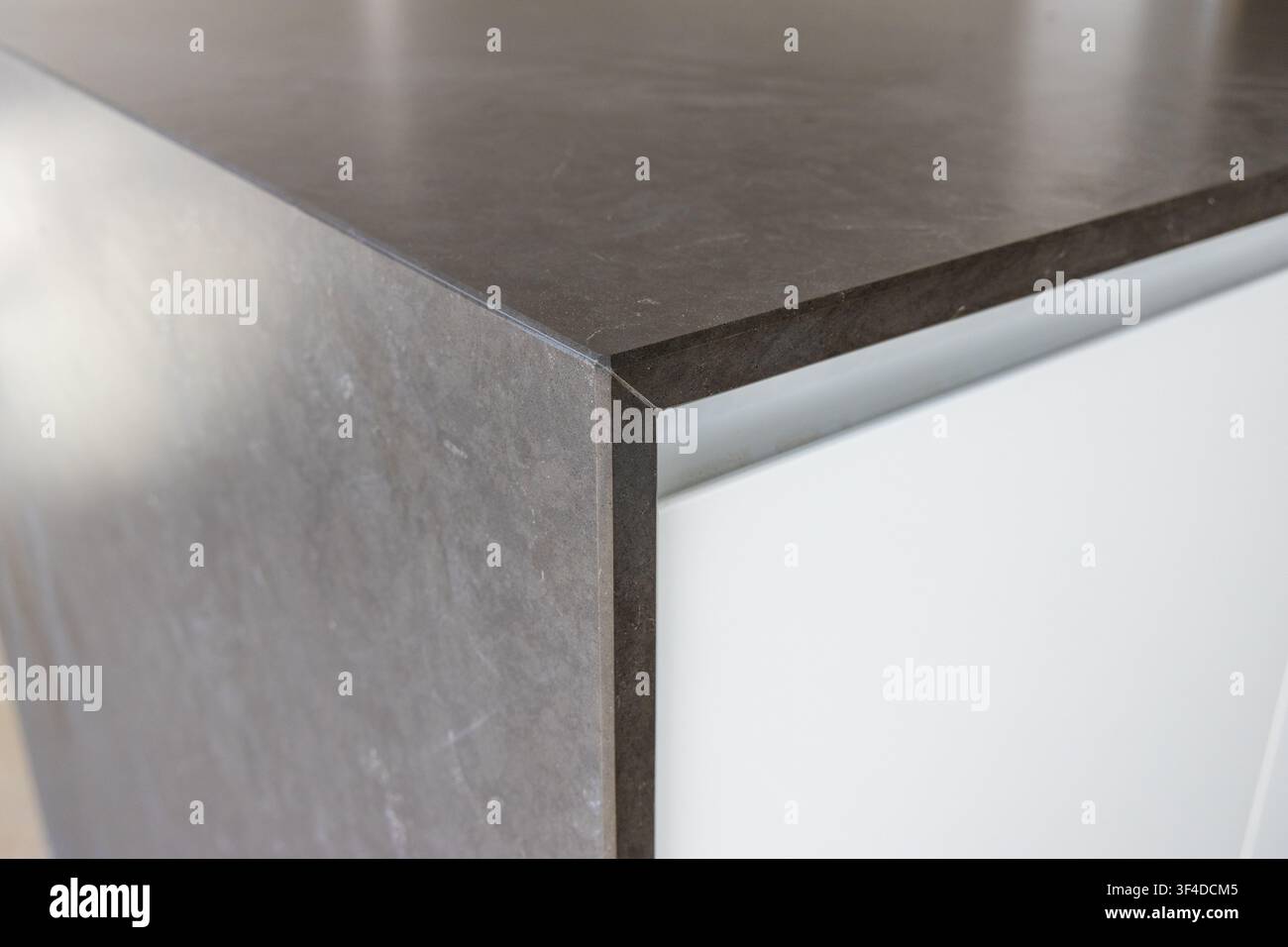 Una vista ravvicinata di un bordo del piano di lavoro in pietra grigio scuro che incontra una superficie di armadio bianca pulita, mostrando il contrasto dei materiali e il design moderno Foto Stock