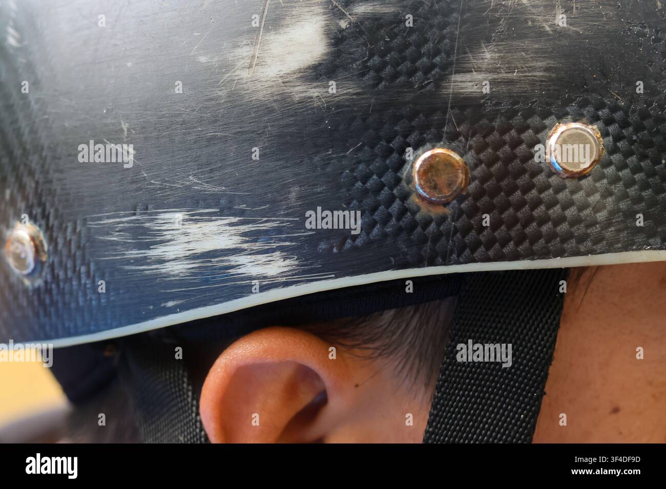 Un casco nero consumato con segni di graffio e rivetti metallici sopra l'orecchio del bambino, che trasmette azione all'aperto e attrezzatura protettiva in uso Foto Stock