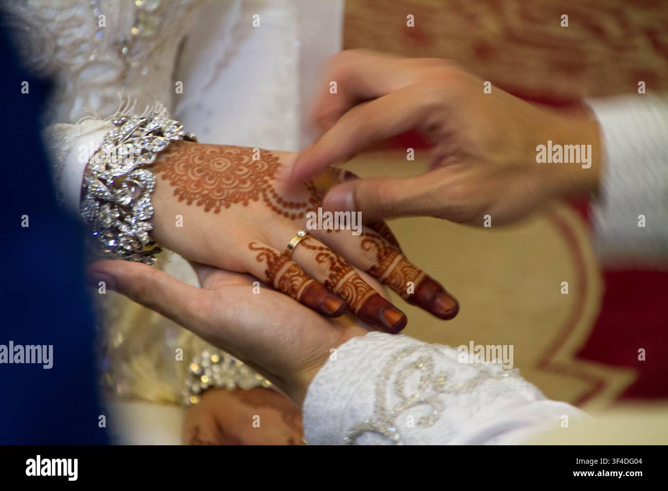 Prima di un fidanzato che infila un anello nuziale d'oro alla mano della sposa, decorata con intricati disegni di henné (mehndi) e un bracciale di diamanti durante una cerimonia nuziale tradizionale. Foto Stock