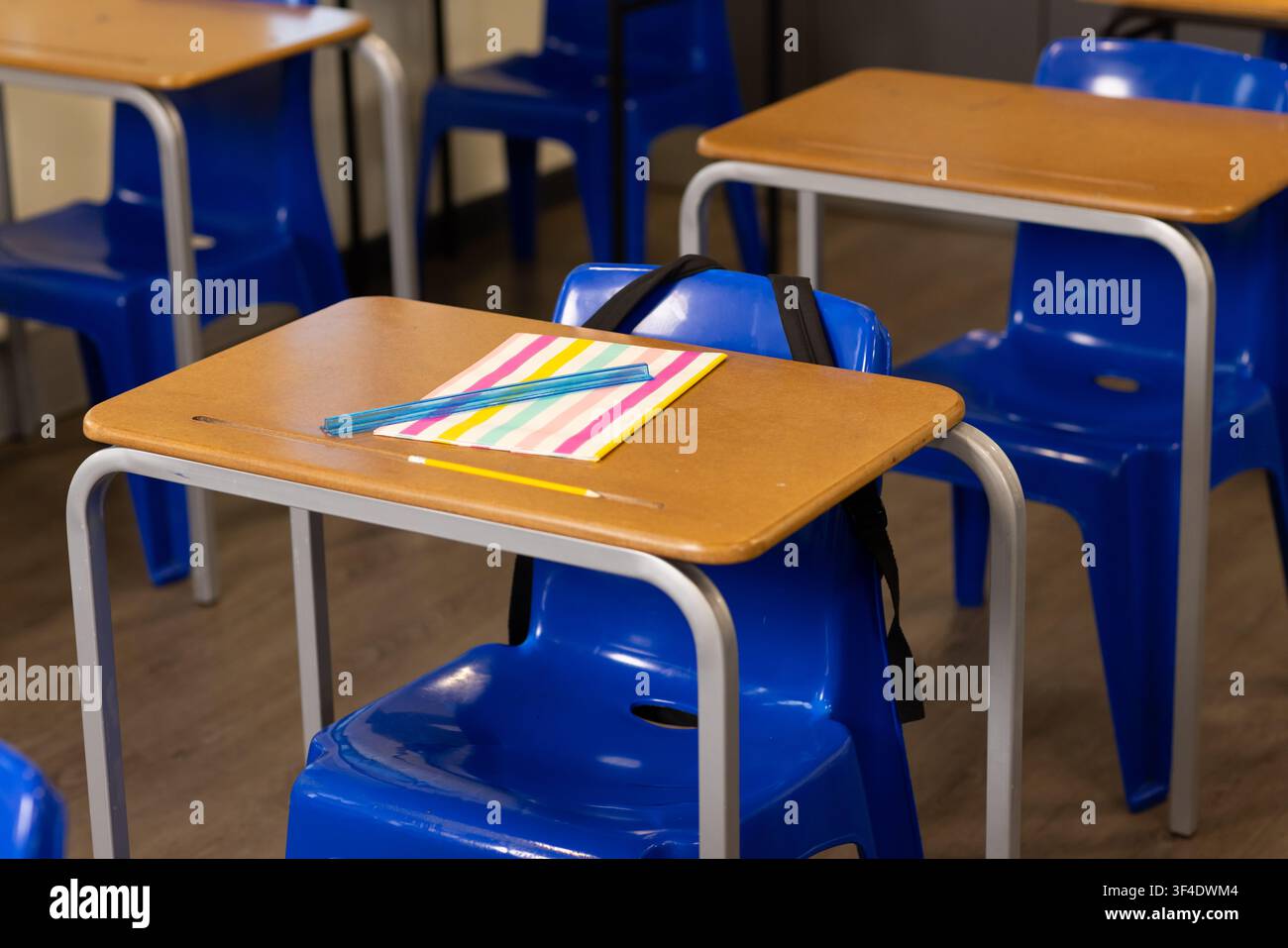 Receptione e sedia blu sedute in aula con quaderno a righe, matita, zaino appeso Foto Stock