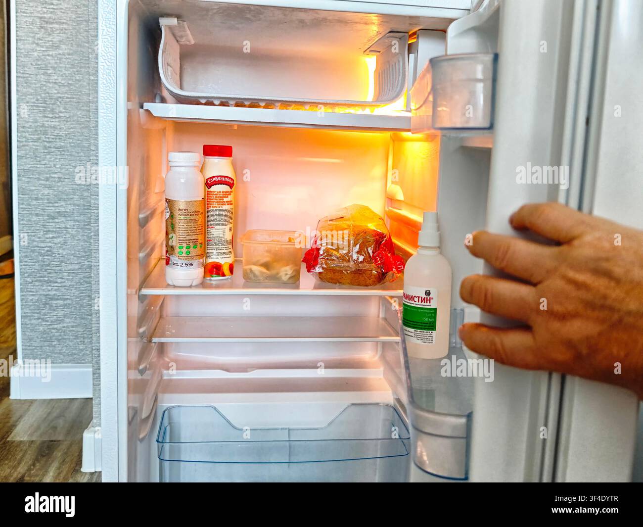 Kirov, Russia – 24 agosto 2025: Una persona raccoglie oggetti all’interno di un frigorifero in una cucina domestica. Il frigo è pieno di bevande, pane e alt Foto Stock