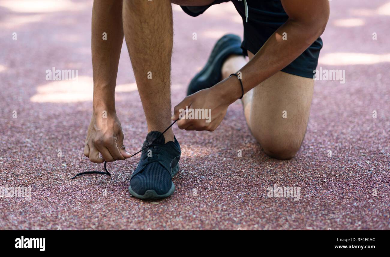 Giovane sportivo che legava le scarpe durante la sua mattina corre all'aperto, vicino alle gambe Foto Stock