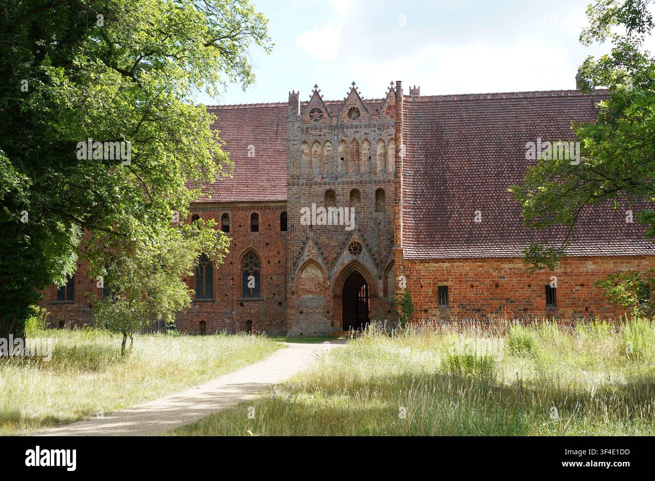 Chorin, Germania - 28 luglio 2026: Architettura gotica in mattoni storica e portale d'ingresso dell'abbazia di Chorin (Kloster Chorin) incorniciati da alberi e vegetazione. Foto Stock