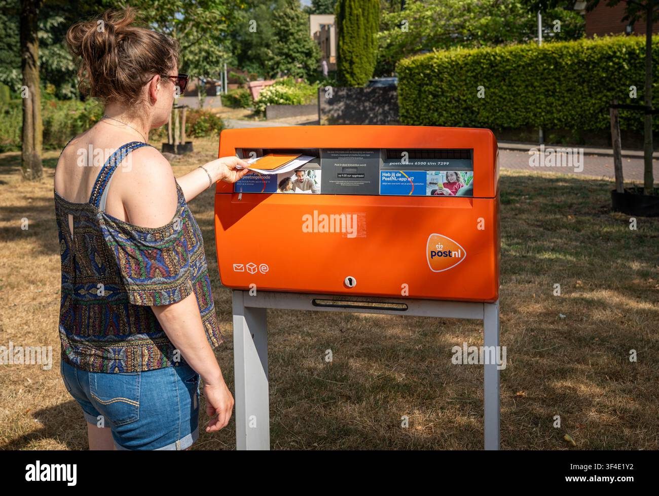 Ede, Paesi Bassi, 25.07.2026, Cassetta delle lettere arancione PostNL con una persona che invia una lettera nei Paesi Bassi Foto Stock