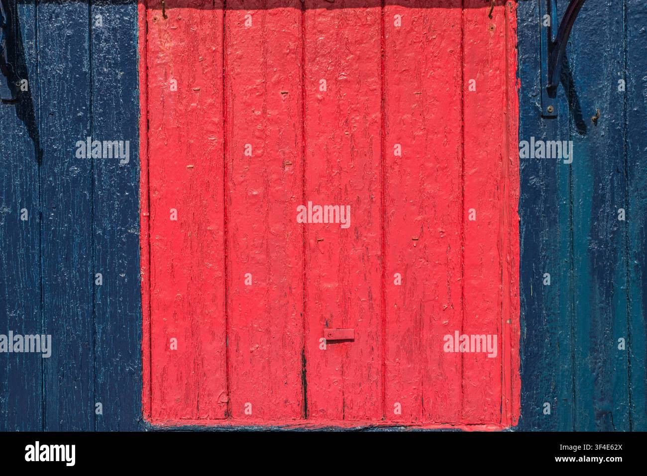Una porta a battente rossa su un capannone di legno blu con vernice scrostata Foto Stock