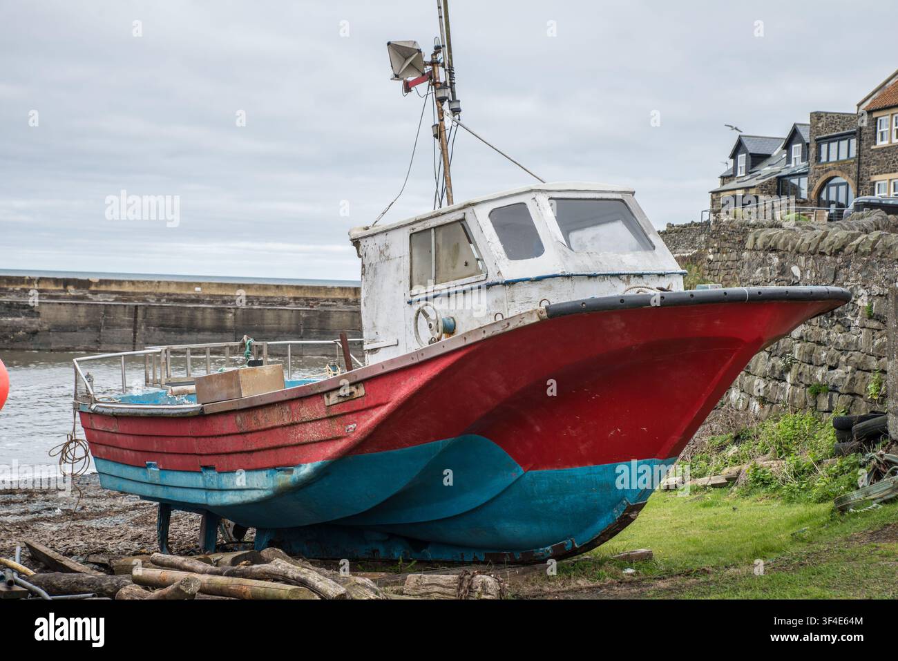 Un piccolo vecchio peschereccio tirato fuori dall'acqua, Craster Harbour, Northumberland, Inghilterra Foto Stock