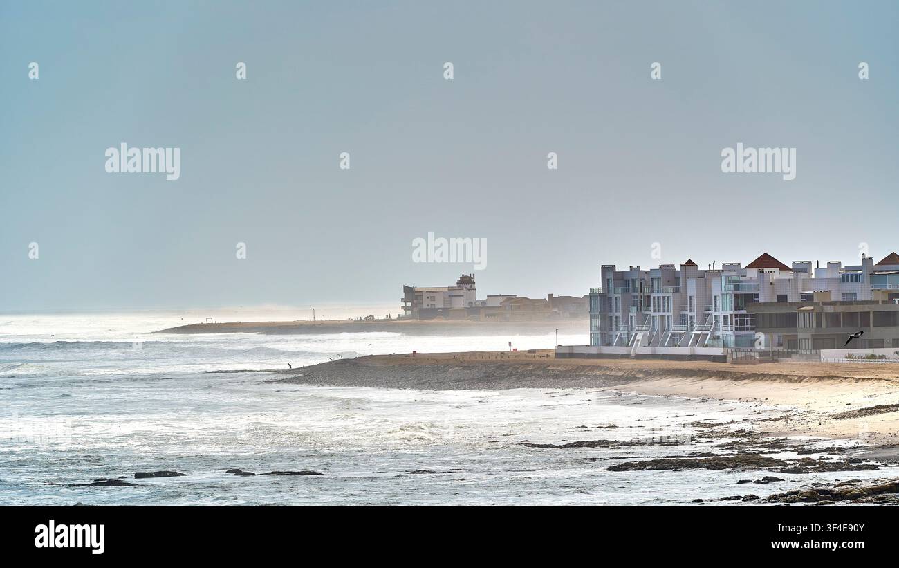 Edifici residenziali moderni lungo la costa atlantica nebbiosa e sferzata dalle onde di Swakopmund, Namibia al mattino presto. Foto Stock