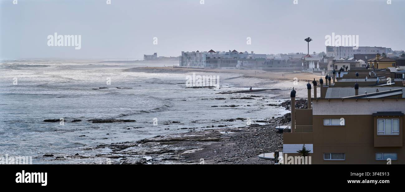 Edifici residenziali moderni lungo la costa atlantica nebbiosa e sferzata dalle onde di Swakopmund, Namibia al mattino presto Foto Stock