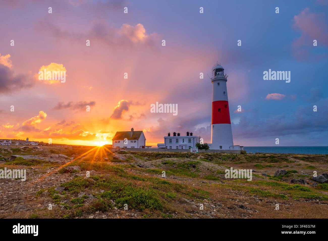 Spettacolare alba con esplosione di stelle accanto al faro di Portland Bill con un cielo mattutino colorato sull'Isle of Portland, Dorset, Inghilterra. Foto Stock