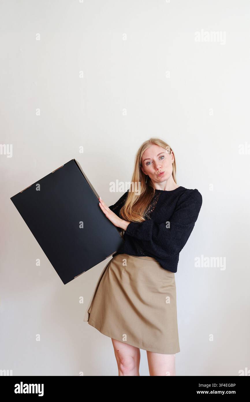 Giovane donna sorridente che tiene una lavagna nera vuota, perfetta per pubblicità, branding, marketing o mockup promozionale. Foto Stock