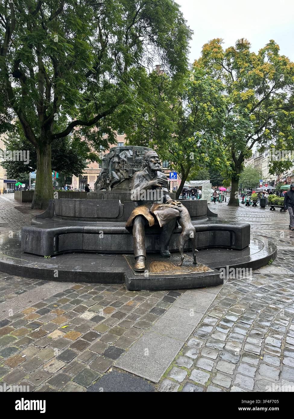 Monumento in bronzo di un uomo seduto con un cane su una piazza di ciottoli. Scultura pubblica in bronzo che raffigura un uomo barbuto seduto e un cane accanto a una pietra f - Immagine stock catturata con smartphone