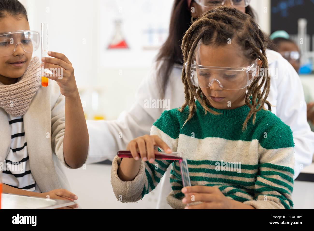 Studenti afroamericani con insegnante che lavorano in un laboratorio scolastico pipettando in una provetta con occhiali protettivi Foto Stock