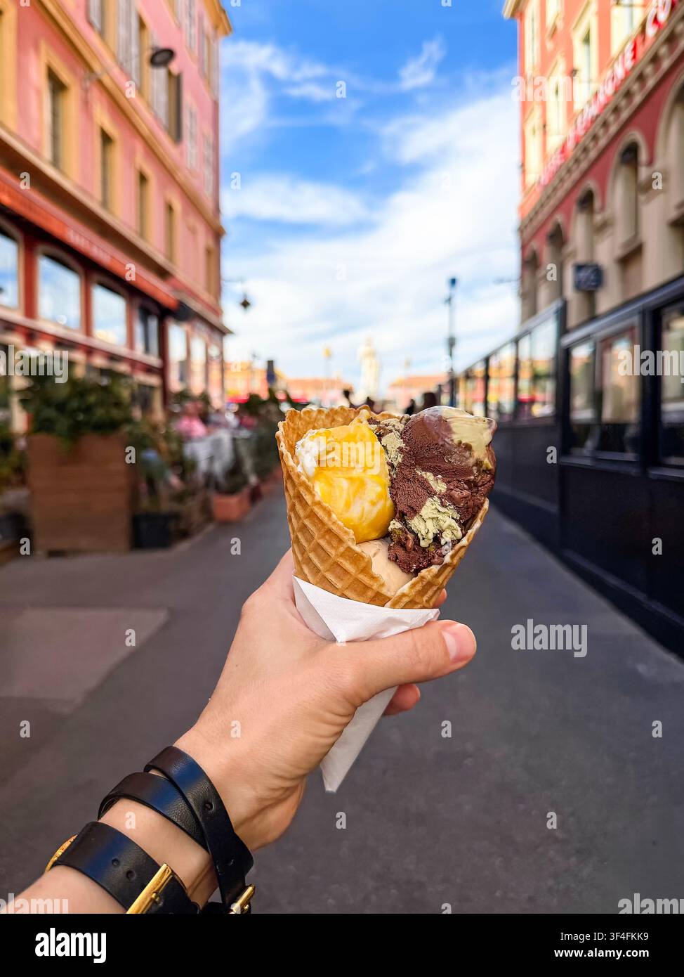 Mano che tiene una cono di waffle con gelato italiano colorato in una strada affascinante del centro storico di Nizza, catturando l'esperienza estiva di viaggio e del cibo locale Foto Stock