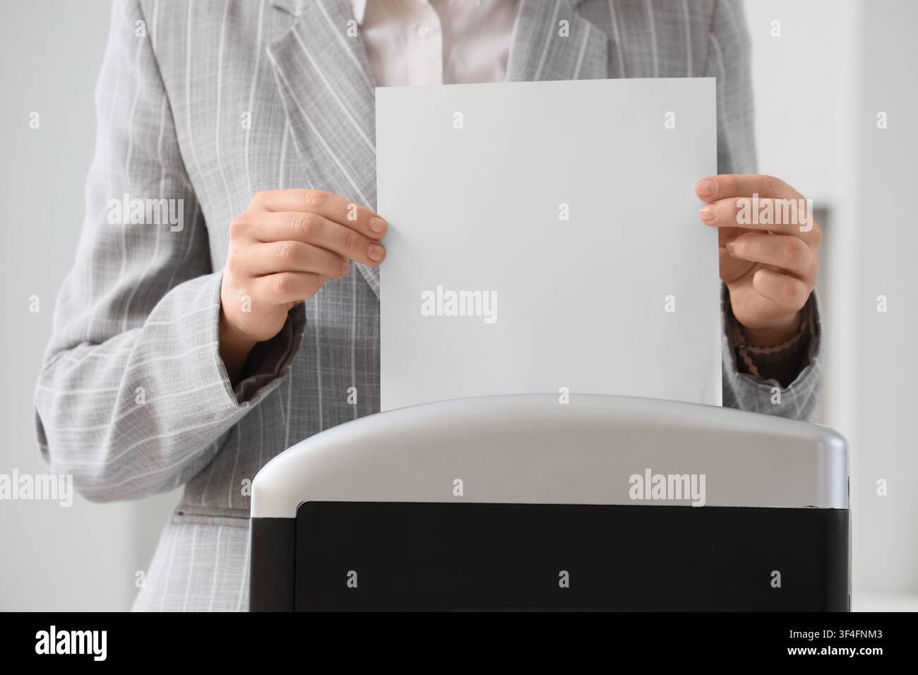 Donna d'affari che distrugge documenti riservati per la protezione dei dati e la privacy in un ambiente d'ufficio, questa azione rappresenta misure di sicurezza per dati sensibili Foto Stock