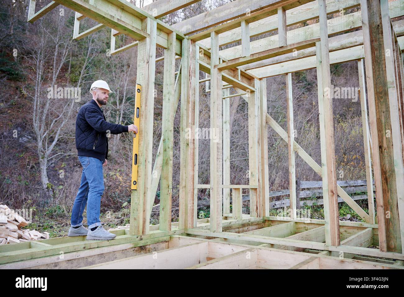 Ingeniero ispeziona una struttura in legno con uno strumento di livellamento nel cantiere, rappresentando lavoro di precisione, stabilità strutturale, garanzia della qualità e processo di sviluppo Foto Stock