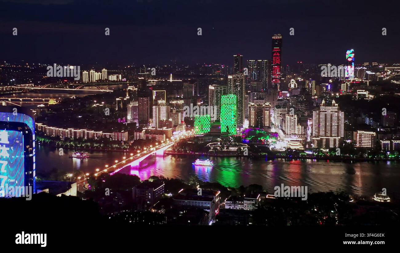 LIUZHOU, CINA - 10 GIUGNO 2024: Una vista aerea notturna che mostra grattacieli colorati illuminati e un ponte luminoso lungo il fiume a Liuzhou, Cina Foto Stock