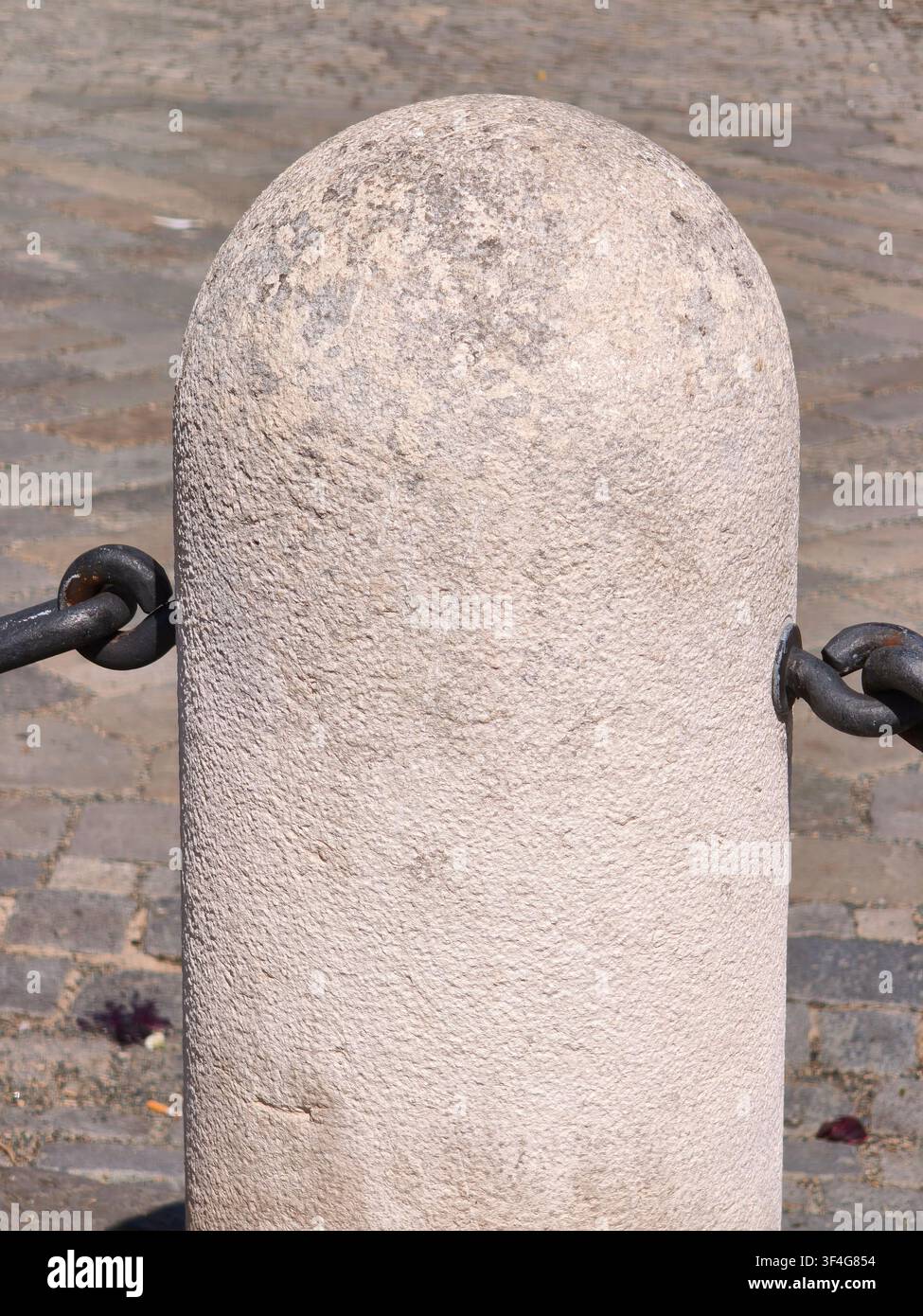 Antico pilastro in pietra con catene di ferro su una strada acciottolata - Immagine stock catturata con smartphone