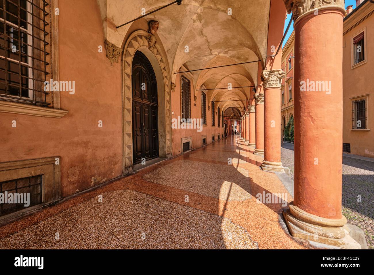 Bologna, Italia - Maggio 2026: Vista prospettica lungo un portico a volta storico con colonne in terracotta e pavimentazione in terrazzo. Foto Stock