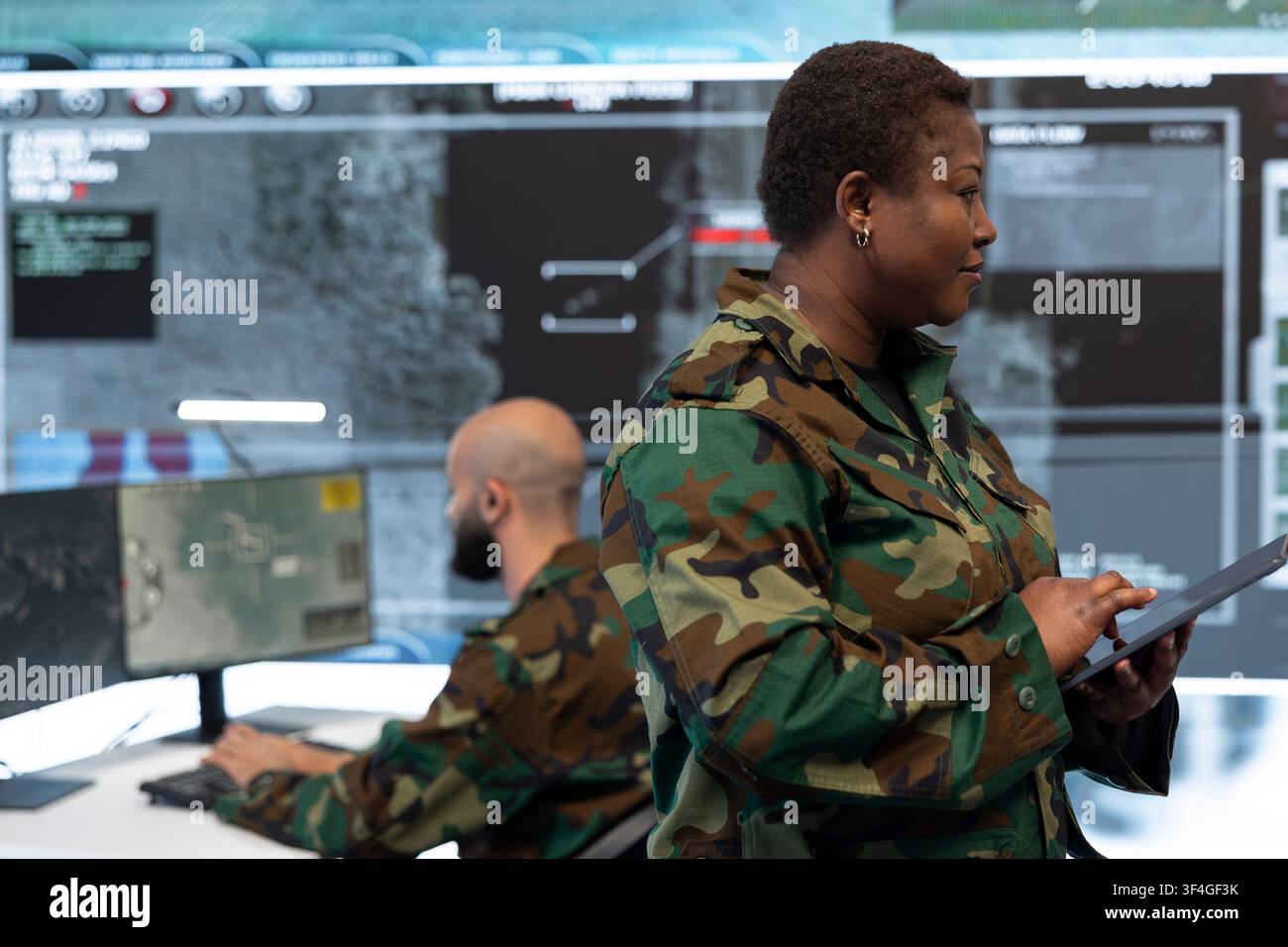 Ufficiale dell'intelligence militare utilizza un tablet mentre cammina nel centro di comando. Donna che lavora come specialista dell'esercito controlla i dati della mappa di guerra sul dispositivo e supervisiona il team Foto Stock