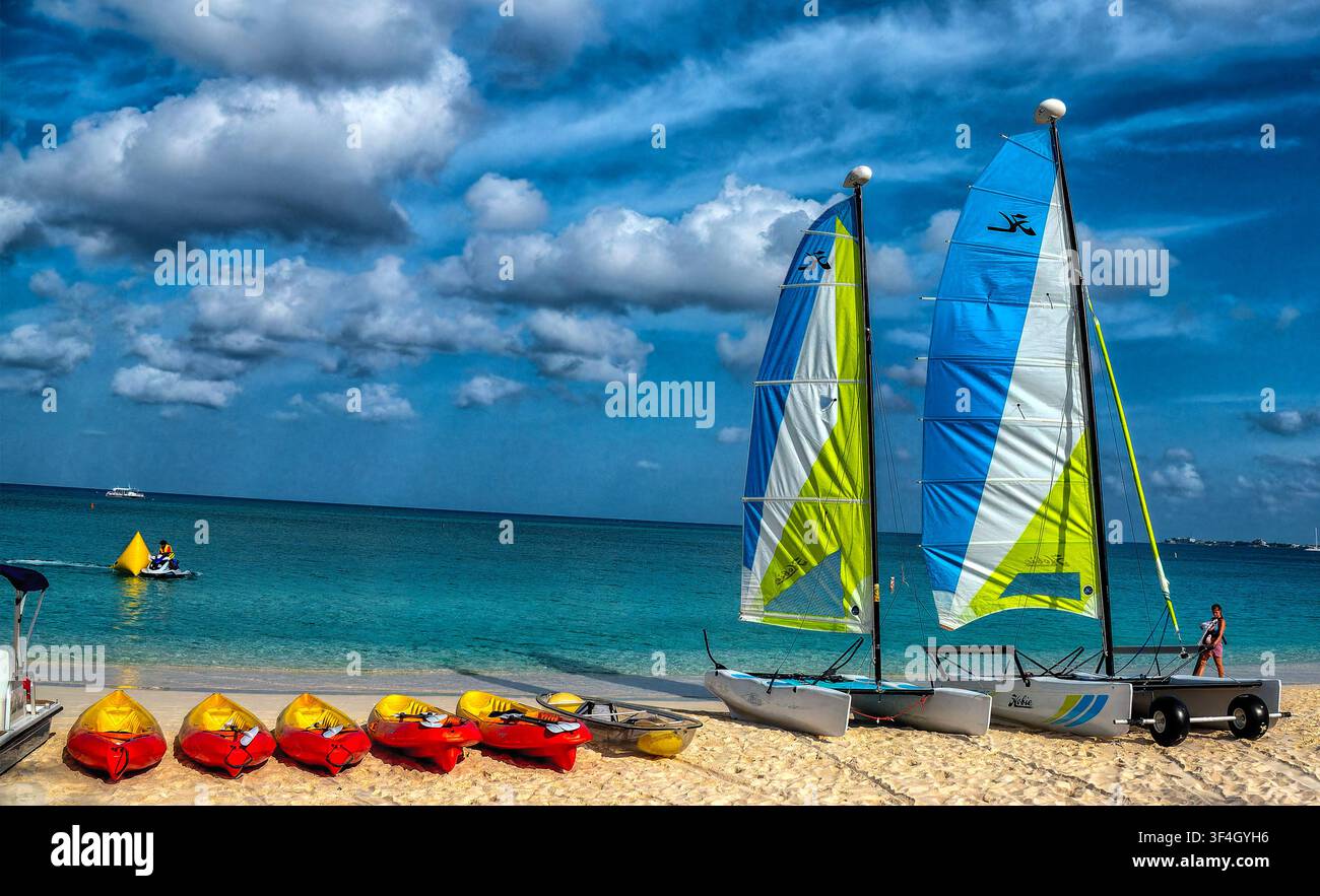 Questa veduta costiera mostra piccoli catamarani ormeggiati sulla riva sabbiosa, con altre barche visibili sull'acqua turchese Foto Stock