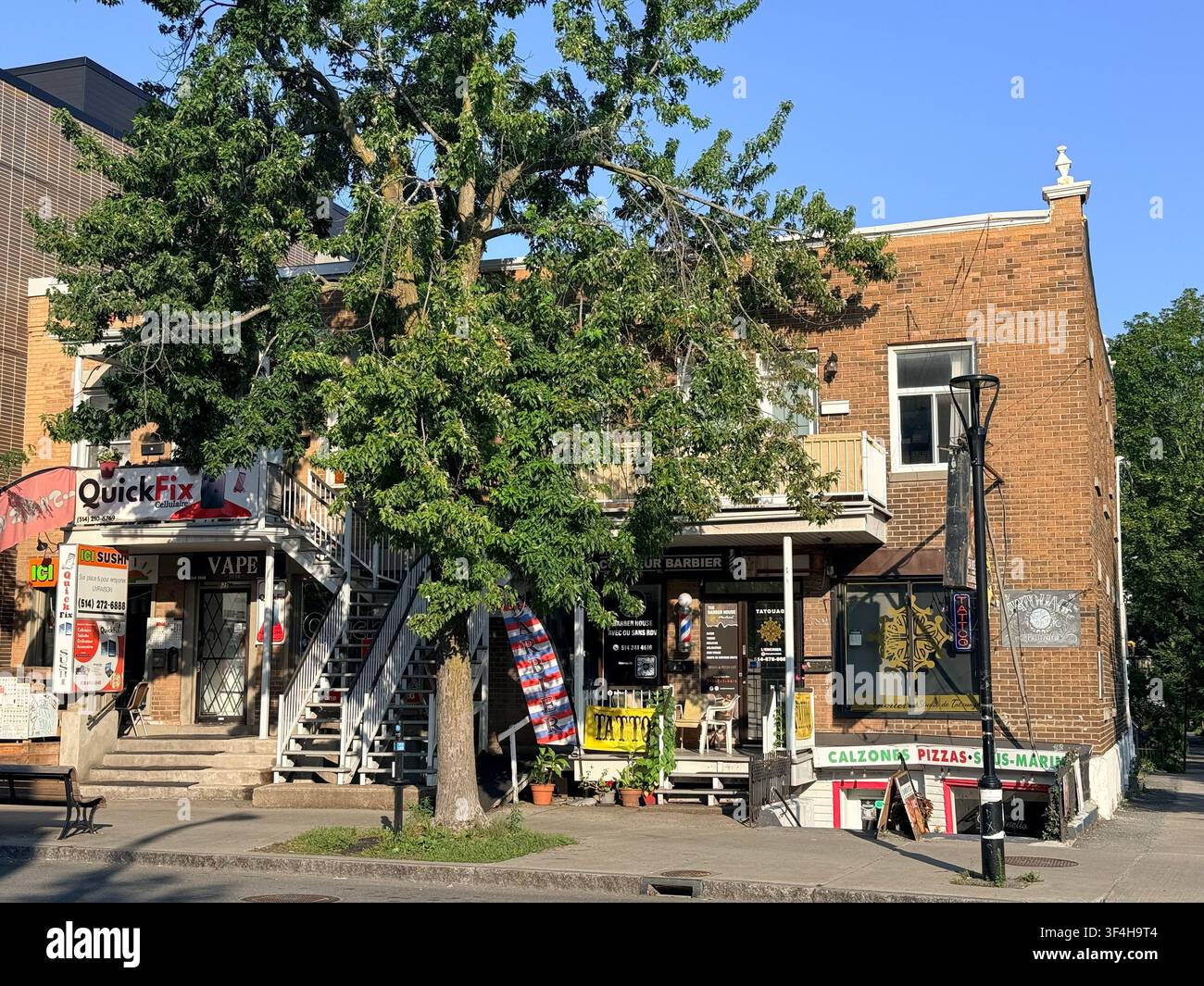 Piccole imprese, un negozio di barbiere e le classiche scale esterne di Montréal costeggiano la via Jarry nel quartiere Villeray di Montréal, Quebec, Canada. - Immagine stock catturata con smartphone