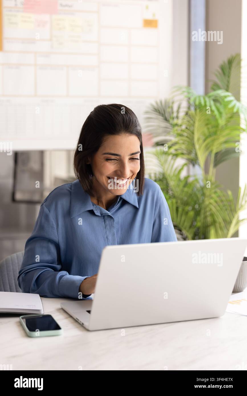 Donna d'affari latina sorridente che lavora online utilizzando un laptop Foto Stock