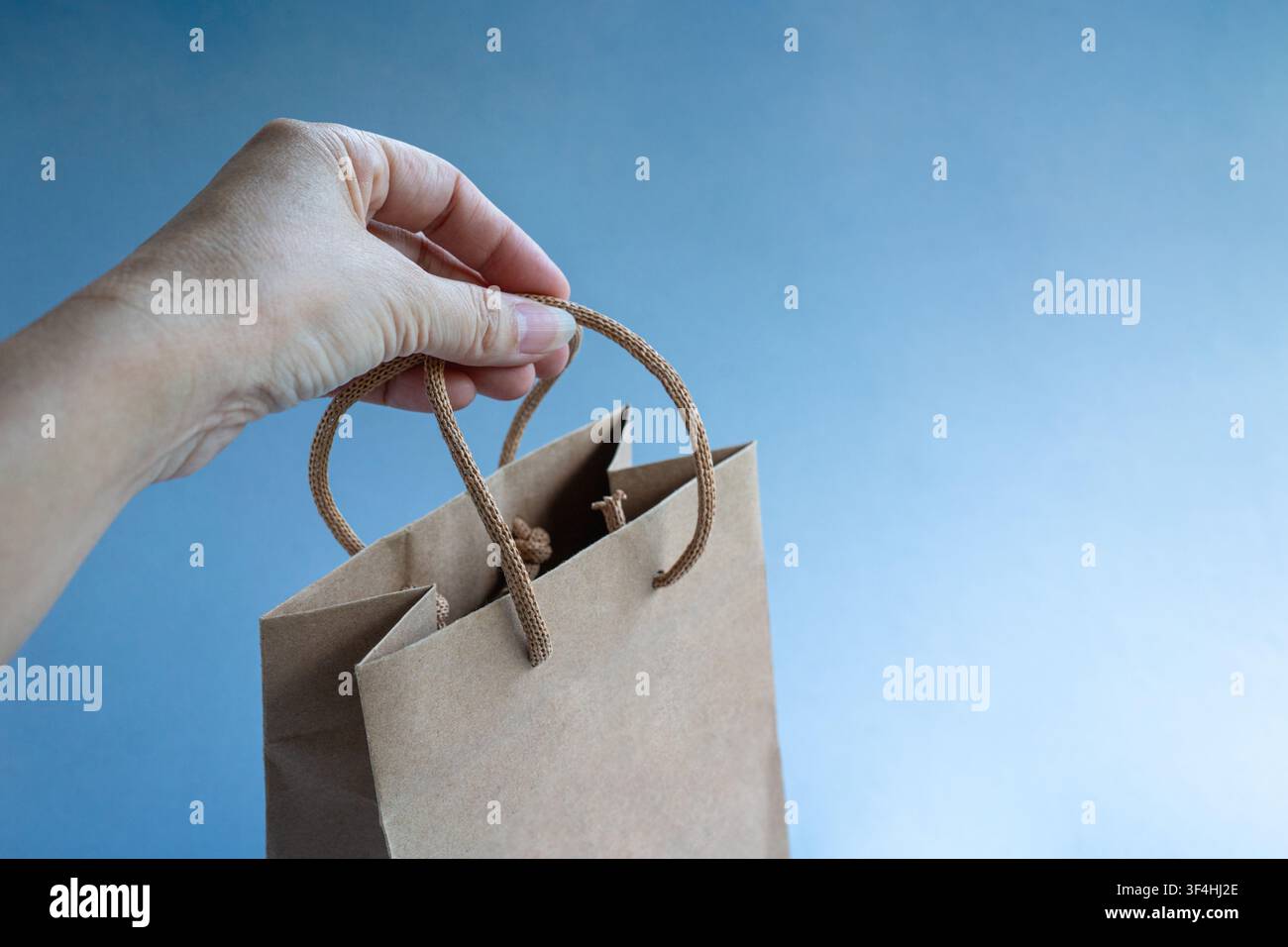 Mano che tiene una borsa della spesa in carta di colore marrone. Isolata su sfondo blu. Foto Stock