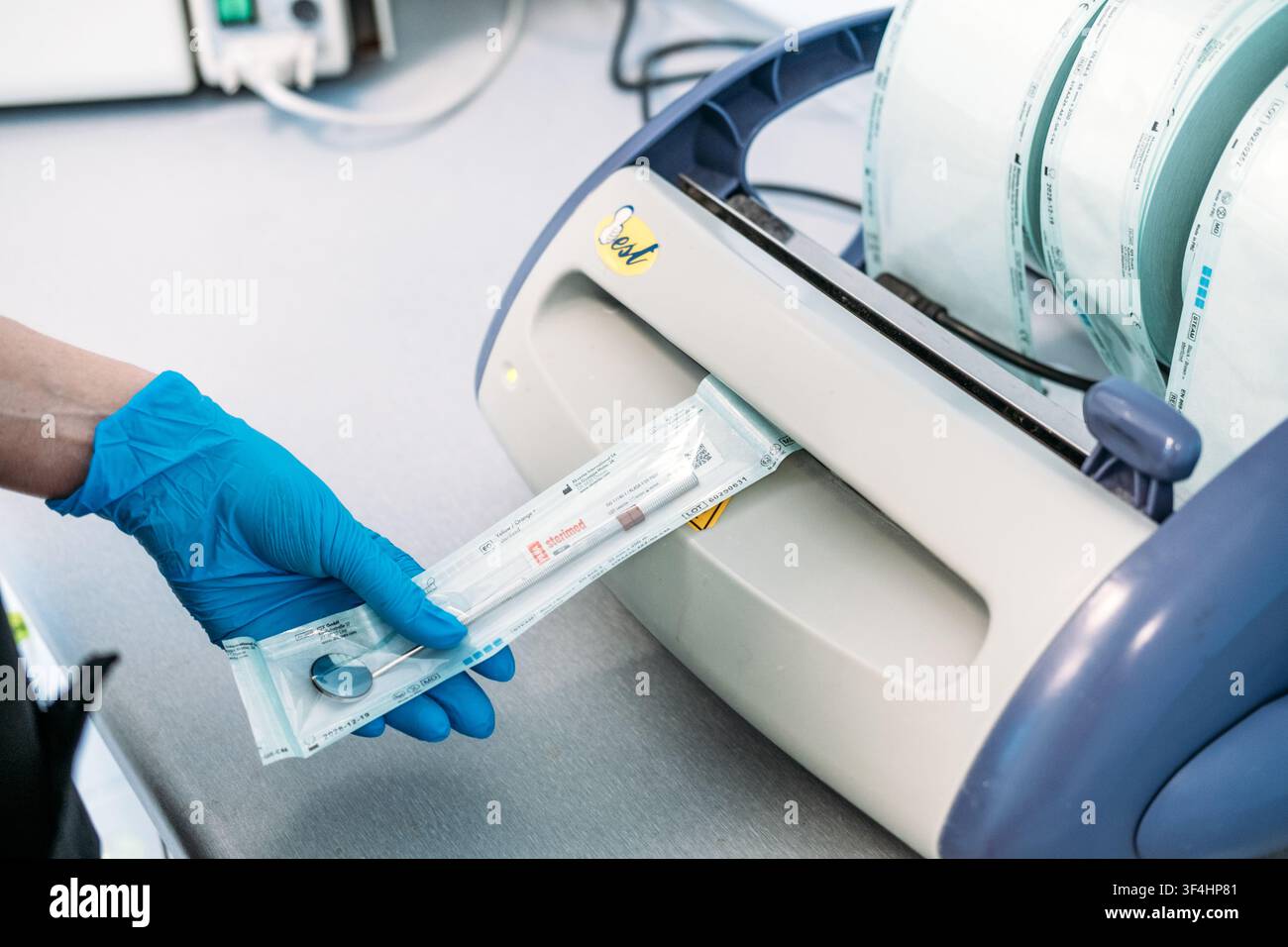 Mani guantate inseriscono una busta trasparente in una macchina di sigillatura sul piano di lavoro in ambito medico. Etichetta di sterilizzazione con numero di lotto, tracciamento del lotto medico Foto Stock
