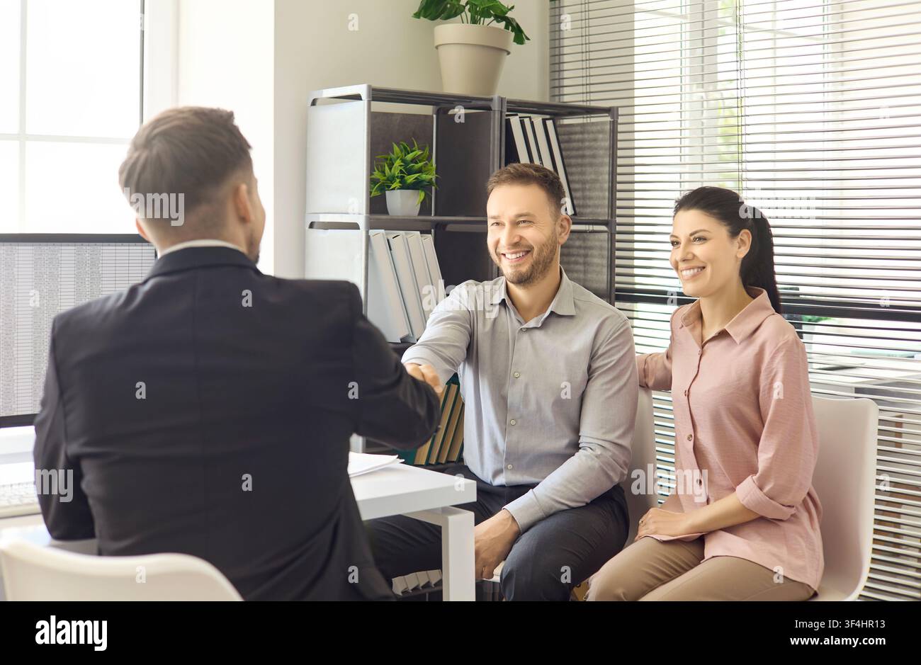 Coppia stringe la mano ad un agente immobiliare in ufficio dopo una consulenza immobiliare riuscita Foto Stock