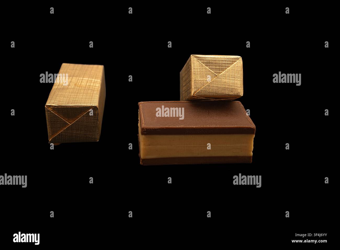 Diverse barrette di cioccolato e involucri disposti ordinatamente su una superficie nera. Gli involucri hanno forme diverse e aggiungono interesse visivo alla composizione. Foto Stock