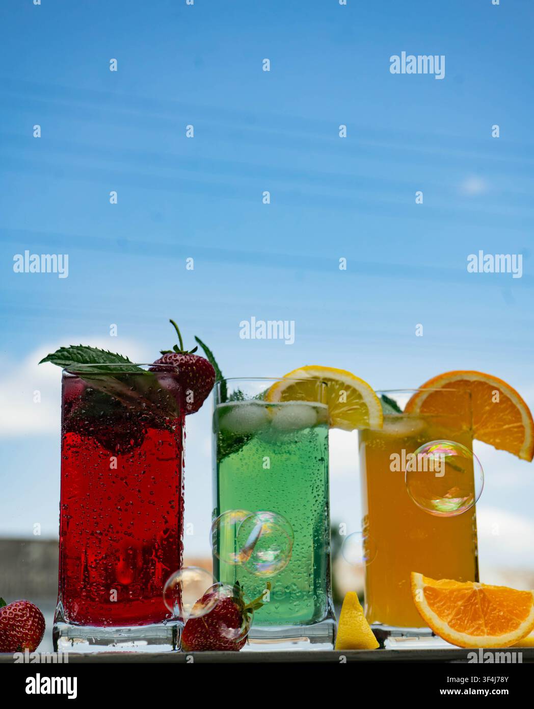 Cocktail estivi rinfrescanti e colorati con agrumi, bacche e menta serviti in bicchieri alti contro un cielo blu luminoso. Bevanda per feste tropicale conce Foto Stock