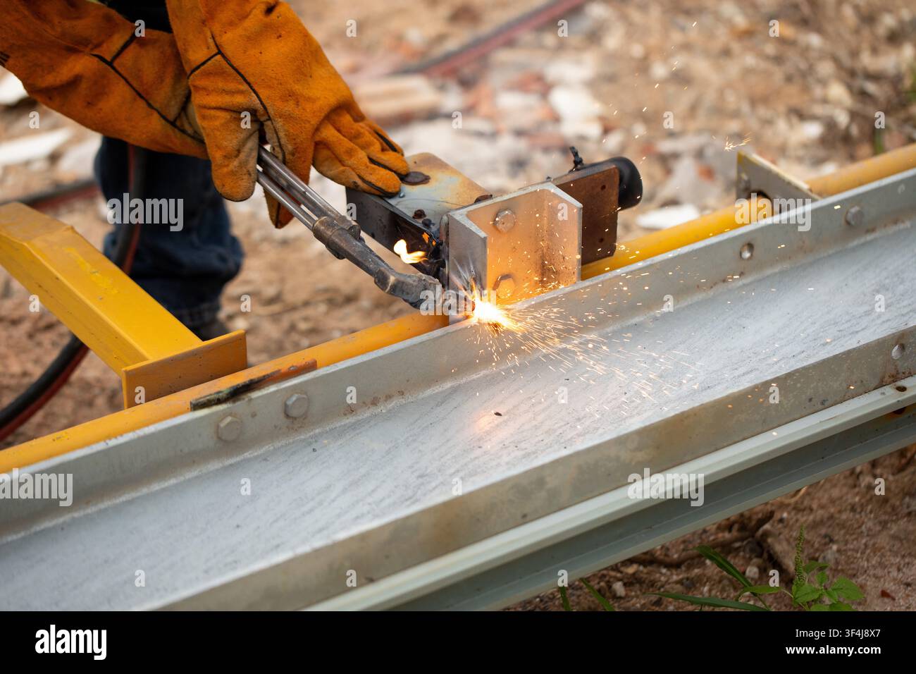 Lavoratore qualificato che taglia con precisione una trave metallica con una fiamma ossidrica, dimostrando la sua abilità artigiana Foto Stock