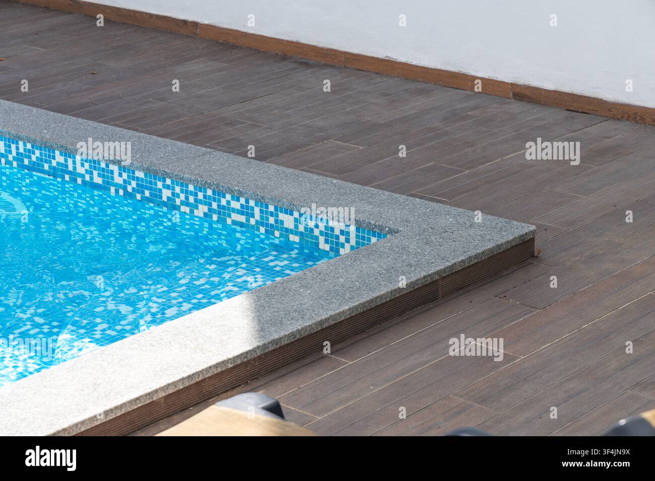 Una vista ravvicinata dell'angolo di una piscina rinfrescante, caratterizzata da piastrelle a mosaico blu brillante e da un bordo in granito strutturato Foto Stock