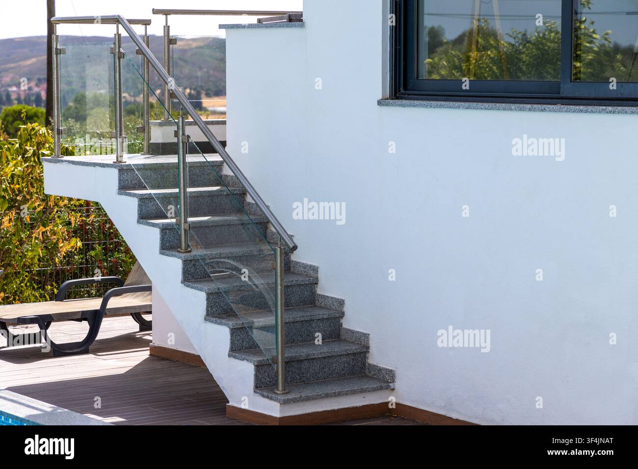 Una scala in granito contemporanea con eleganti ringhiere in metallo e vetro si innalza accanto a un muro in stucco bianco Foto Stock