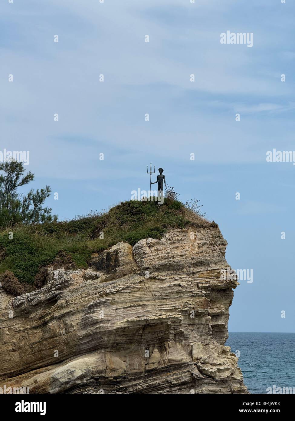 Statua di Neptuno Nino che tiene un tridente sopra una roccia costiera stratificata a Santander, in Spagna. - Immagine stock catturata con smartphone