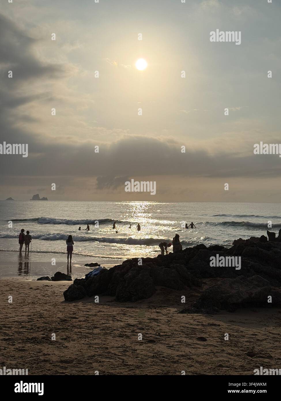 Persone in silhouette sulla costa atlantica sotto nuvole scure di pioggia al tramonto a Santander, Cantabria, Spagna - Immagine stock catturata con smartphone