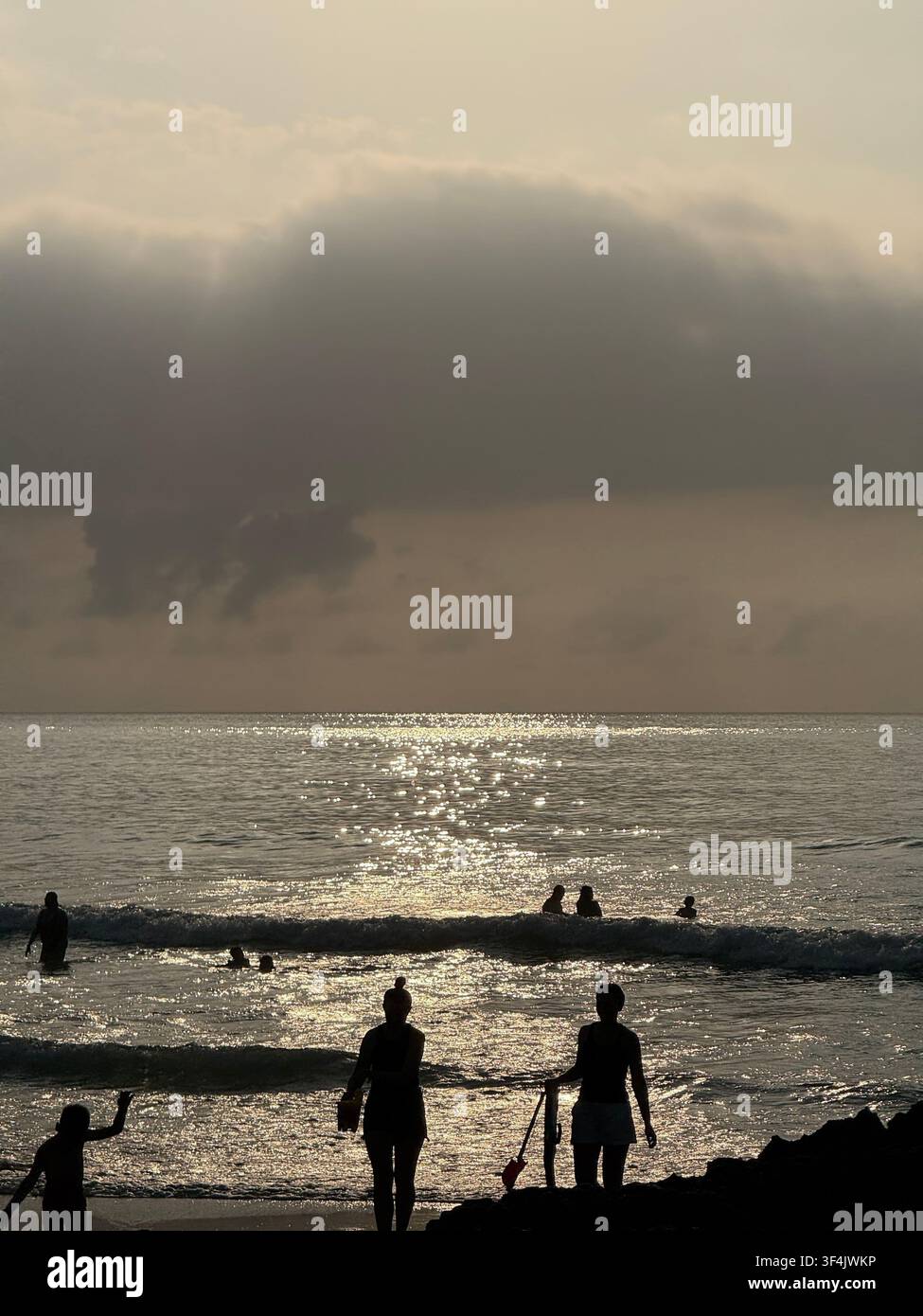 Persone in silhouette sulla costa atlantica sotto nuvole scure di pioggia al tramonto a Santander, Cantabria, Spagna - Immagine stock catturata con smartphone