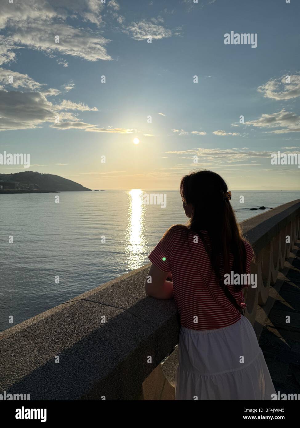 Donna che guarda l'Oceano Atlantico da una passeggiata costiera al tramonto ad A Coruña, Galizia, Spagna - Immagine stock catturata con smartphone