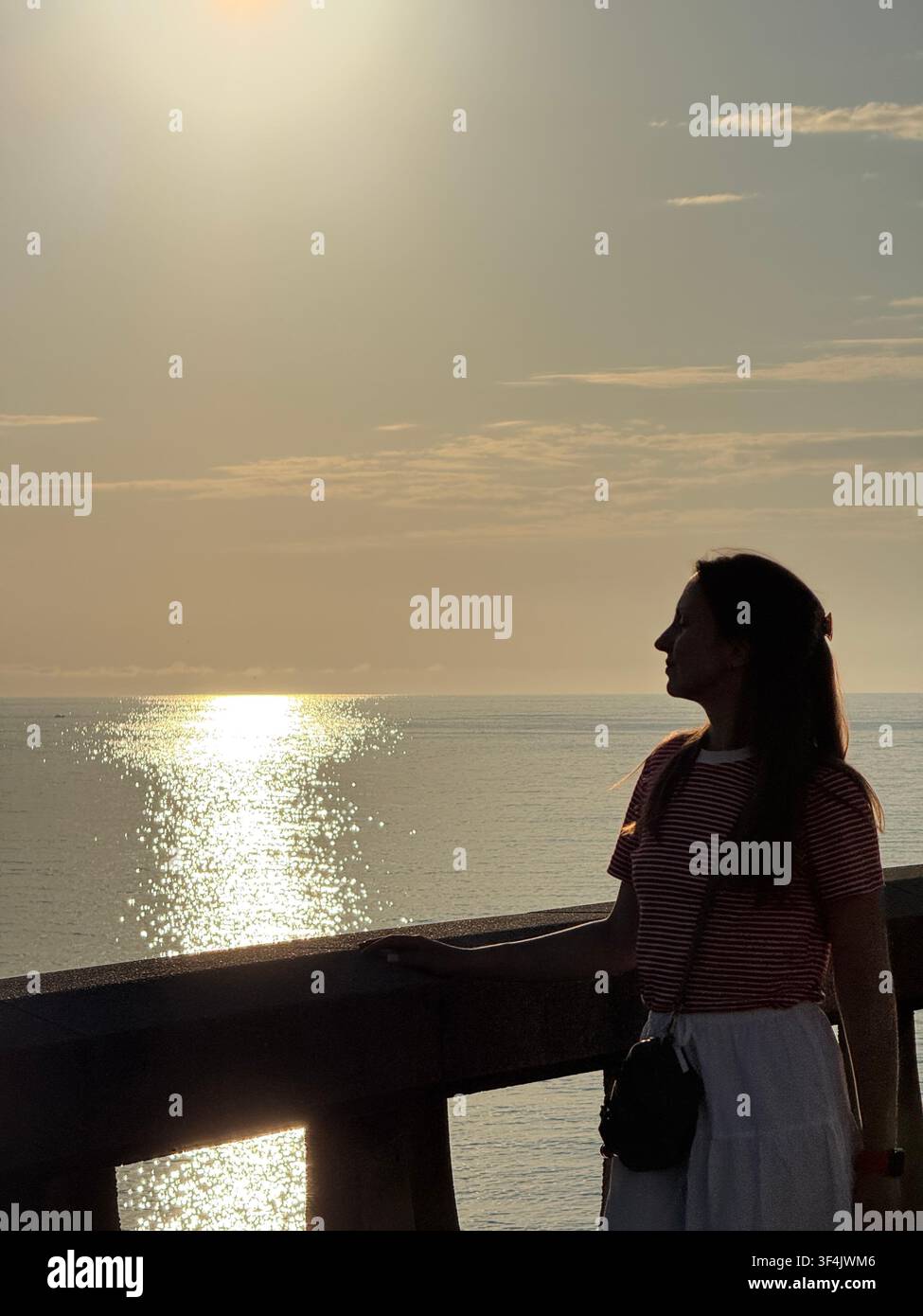 Donna che guarda l'Oceano Atlantico da una passeggiata costiera al tramonto ad A Coruña, Galizia, Spagna - Immagine stock catturata con smartphone