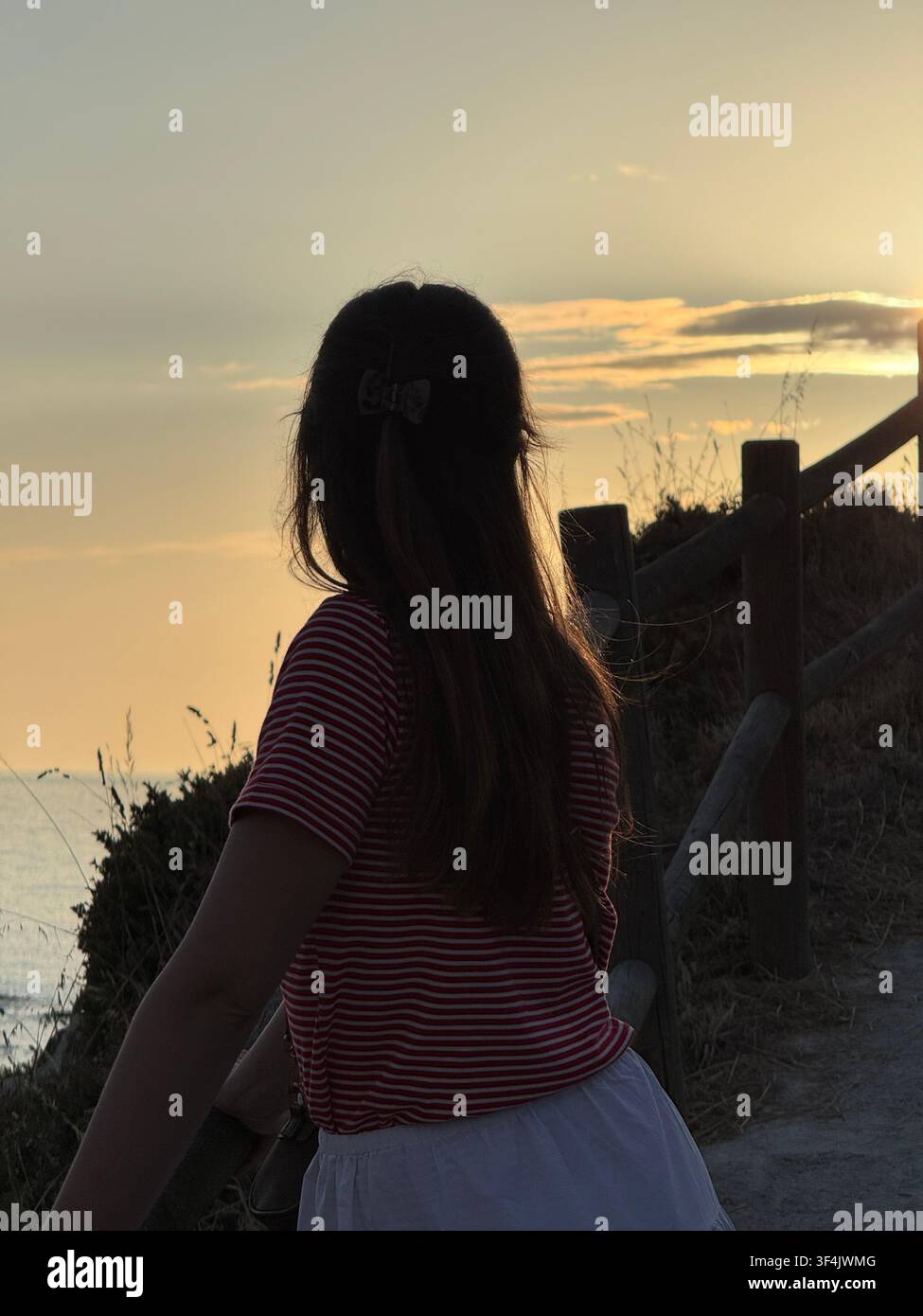 Donna che guarda l'Oceano Atlantico da una passeggiata costiera al tramonto ad A Coruña, Galizia, Spagna - Immagine stock catturata con smartphone